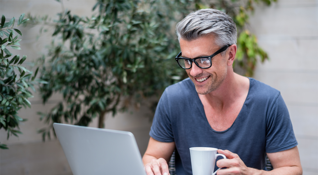 Older man happy with full head of hair working on his laptop.