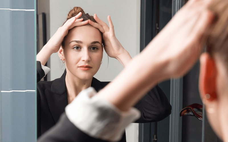 Photo of woman examining her hair line in the mirror.
