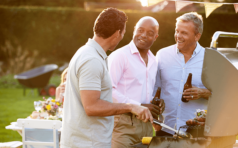 Older men talking around a grill.